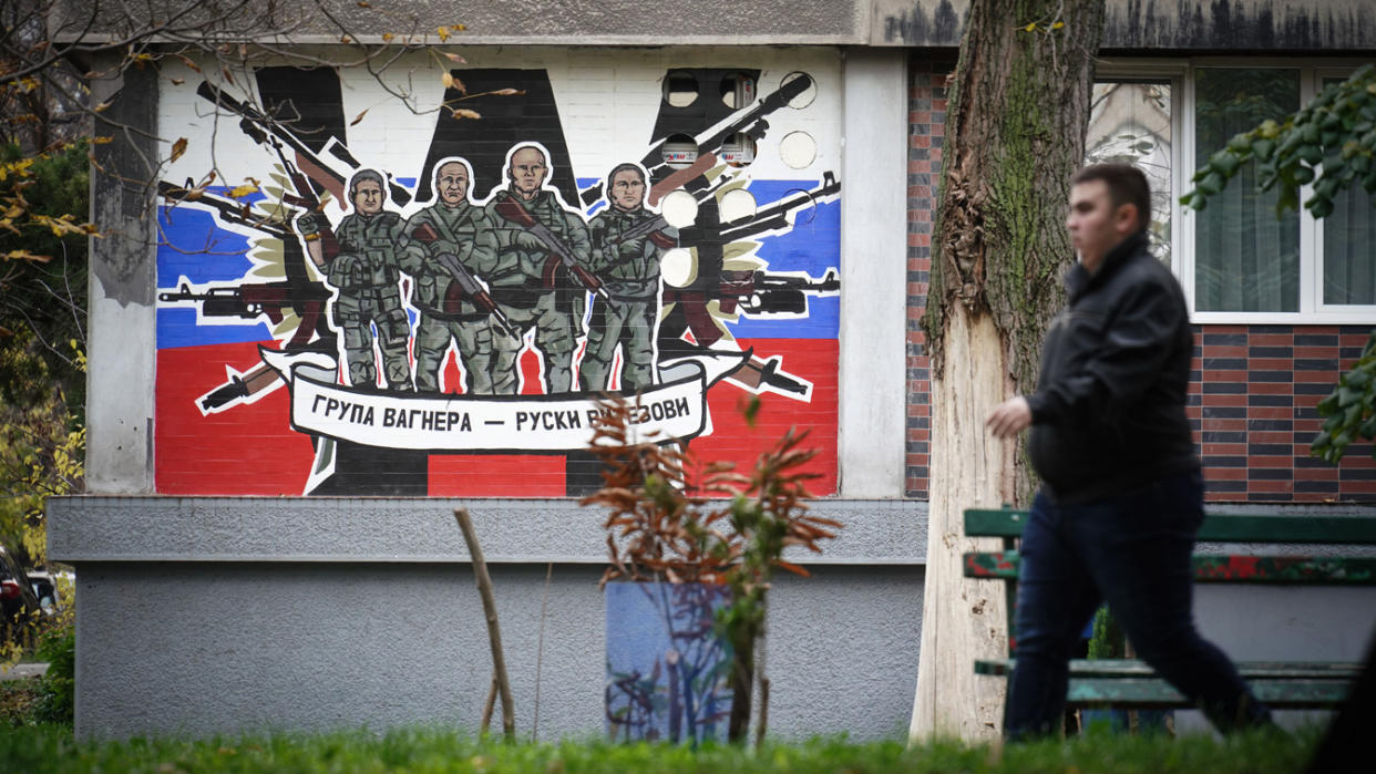 A pedestrian walks past a mural showing four mercenaries of the Wagner Group getting ready to fire their weapons.