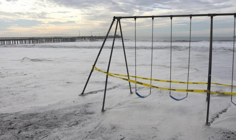 Caution tape marks off the swingset at Avila Beach as high surf pounds the pier and coast on Thursday, Dec. 28 2023.