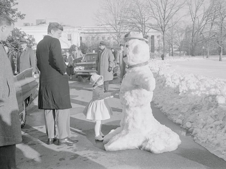 President John F. Kennedy and his three-year-old daughter Caroline pause to examine a five-foot snowman built by Robert Redman, Chief White House gardener, as they arrived at the White House.
