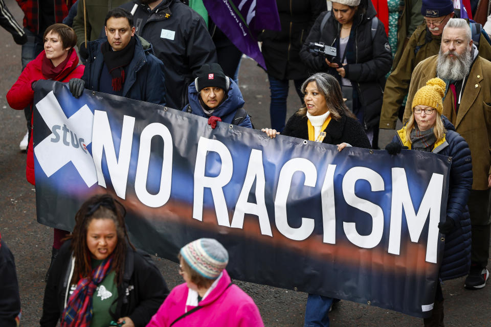 People hold up a "No Racism" banner at a rally