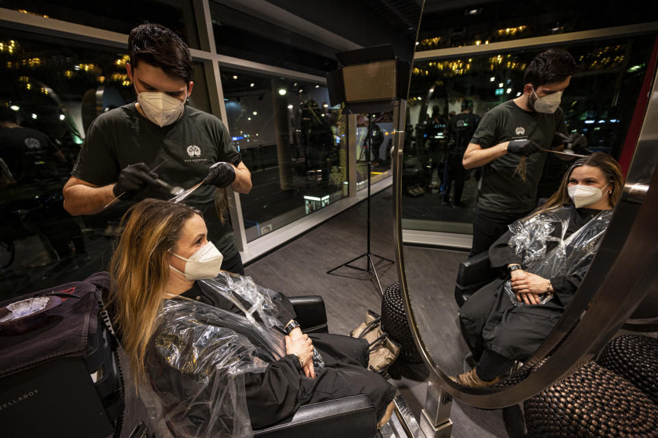 The first customer of Shan Rahimkhan's barbershop gets her hair cut and colored after the reopening in Berlin, Germany, early Monday, March 1, 2021. Hairdressers welcome customers in Germany after successfully lobbying the government to be allowed to reopen their doors while hospitality business and shops remain closed to battle the coronavirus pandemic. (Fabian Sommer/dpa via AP)