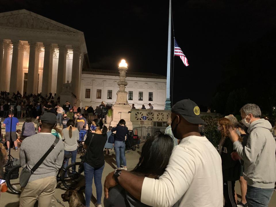 Kent Campbell, 34, and Mekita Rivas, 30. pictured from behind, look on at the somber scene outside the U.S. Supreme Court on Friday night. The couple had just eaten dinner when they heard the news about Ruth Bader Ginsburg's death, and they immediately went to the courthouse to pay their respects.