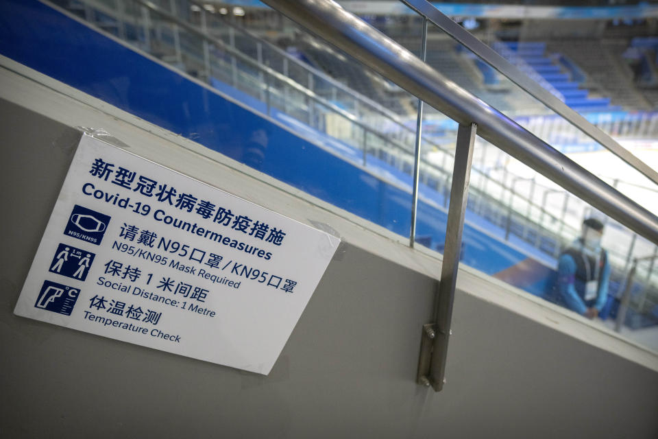 FILE - A staff member stands near a sign outlining COVID-19 protection measures during the Experience Beijing Ice Hockey Domestic Test Activity, a test event for the 2022 Beijing Winter Olympics, at the National Indoor Stadium in Beijing, on Nov. 10, 2021. The prevention protocols will be similar to those at the Tokyo Games this summer, but tighter. It won't be a stretch for Beijing organizers, with China having maintained its zero-tolerance policy to the virus nationally since early in the pandemic. (AP Photo/Mark Schiefelbein, File)