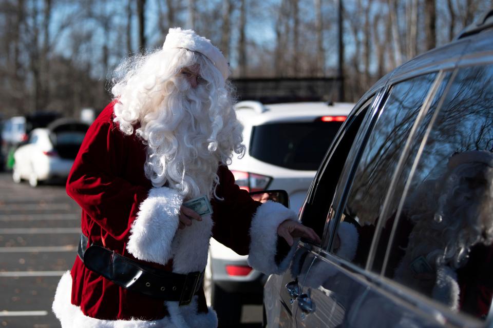 A community member dressed up as Santa Claus gives out cash donated by philanthropist Gene Epstein at Bucks County Community College's Bristol campus on Friday, Dec. 9, 2022. Epstein gave out $100 each to around 500 people as they came to pick up fresh produce from the Fresh Connect program that provides fruit and vegetables free to those in need.