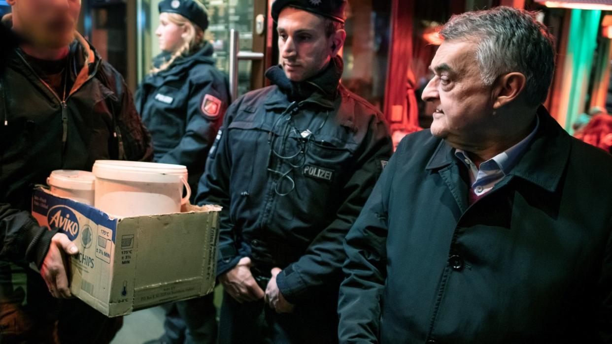 Herbert Reul (r), Innenminister von Nordrhein-Westfalen, verfolgt, wie nach einer Razzia Beweismittel aus einer Shisha-Bar getragen werden. Foto: Bernd Thissen