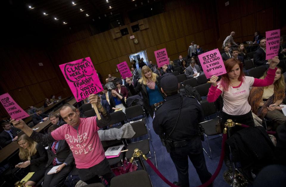 A Capitol Police officer monitors members of Code Pink as they hold up signs on Capitol Hill in Washington, Wednesday, Jan. 29, 2014, before the arrival of Director of National Intelligence James Clapper who testified before the Senate Intelligence Committee hearing on current and projected national security threats against the US. (AP Photo/Pablo Martinez Monsivais)