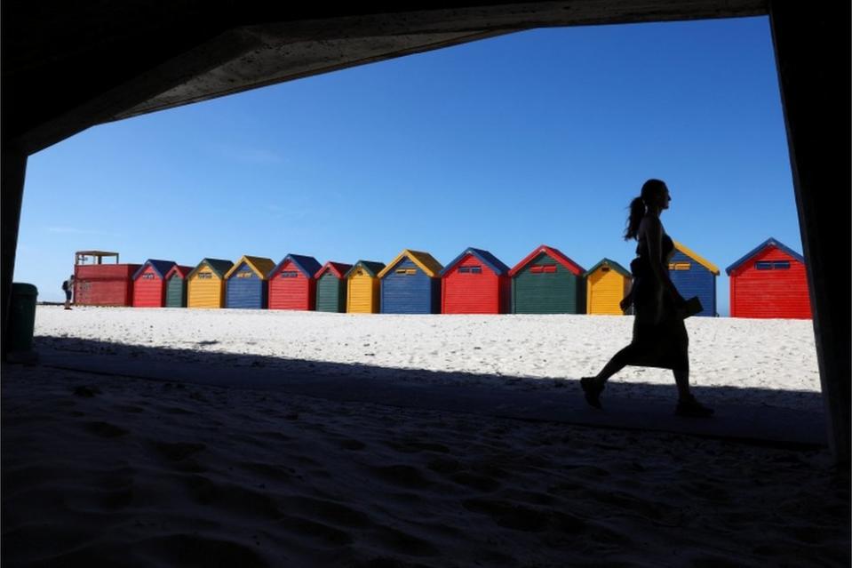 A woman walks past colourful beach huts.