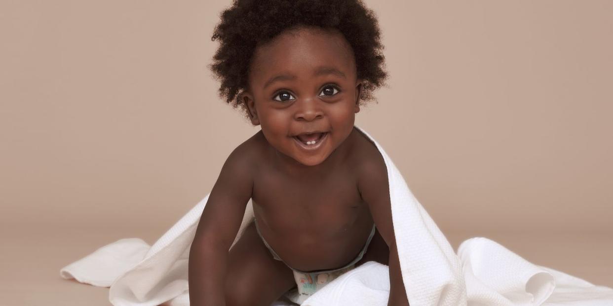 cute baby with afro hair and a white blanket smiling at the camera