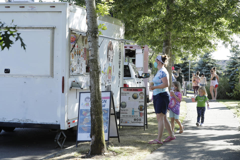 Customers line up to order from the YS Street Food food truck, Monday, Aug. 10, 2020, near the suburb of Lynnwood, Wash., north of Seattle. Long seen as a feature of city living, food trucks are now finding customers in the suburbs during the coronavirus pandemic as people are working and spending most of their time at home. (AP Photo/Ted S. Warren)