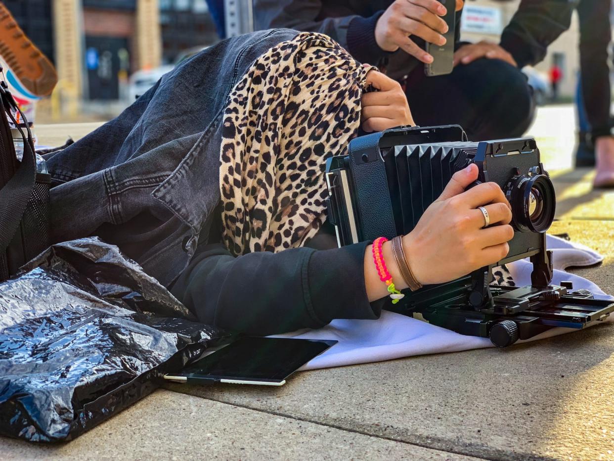 The author covers her head while shooting with a film camera while another person shoots with their phone behind her