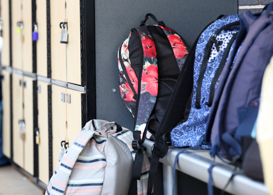 Students' backpacks sitting on a hallway floor.