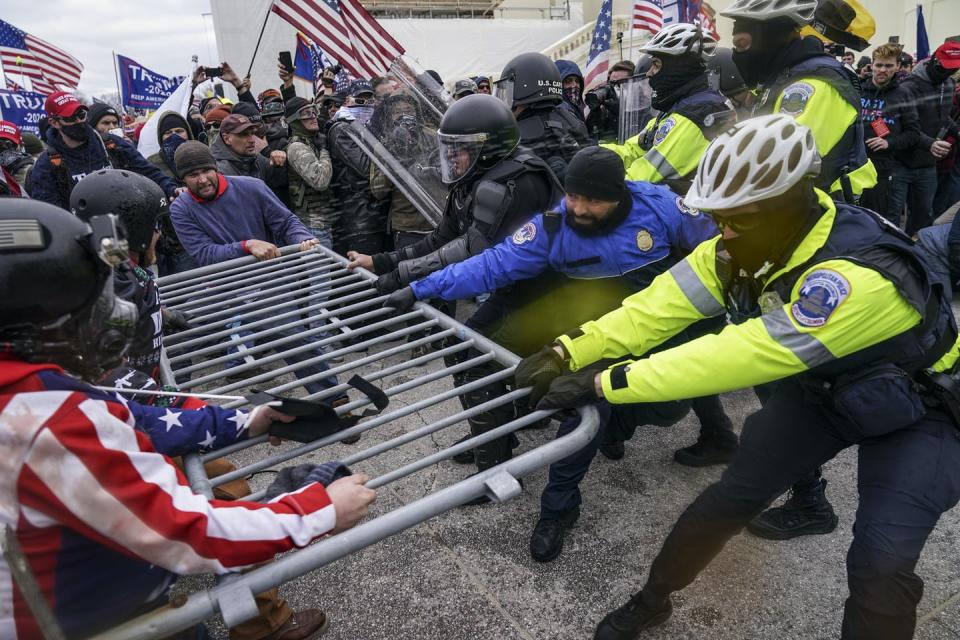 Police and protesters engage in a tug of war over a metallic barrier.