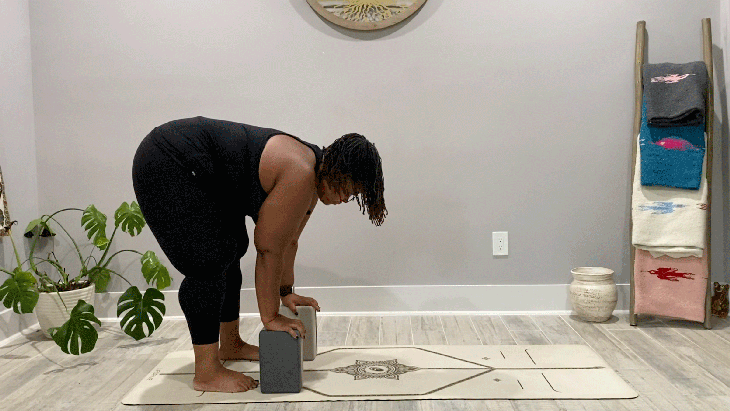 Woman standing on a yoga mat in a forward bend with her hands on blocks
