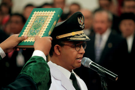 FILE PHOTO: A man holds a Koran as Jakarta Governor Anies Baswedan stands during a swearing-in ceremony at the Presidential Palace in Jakarta, Indonesia, October 16, 2017. REUTERS/Beawiharta/File Photo