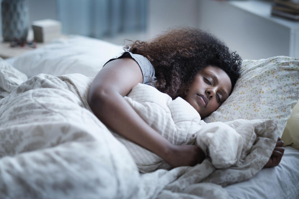 Person sleeping peacefully on a bed with a white comforter and patterned sheets