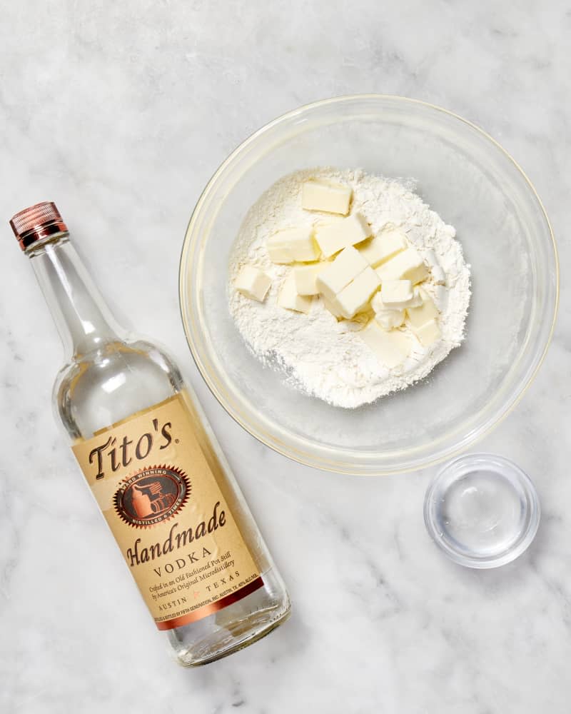 A bowl with flour and cubes of butter and a bottle of vodka to make a pie crust seen from above.