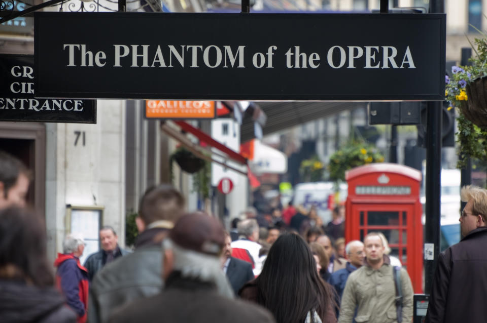 Phantom of the Opera sign in London as people walk on the street below it