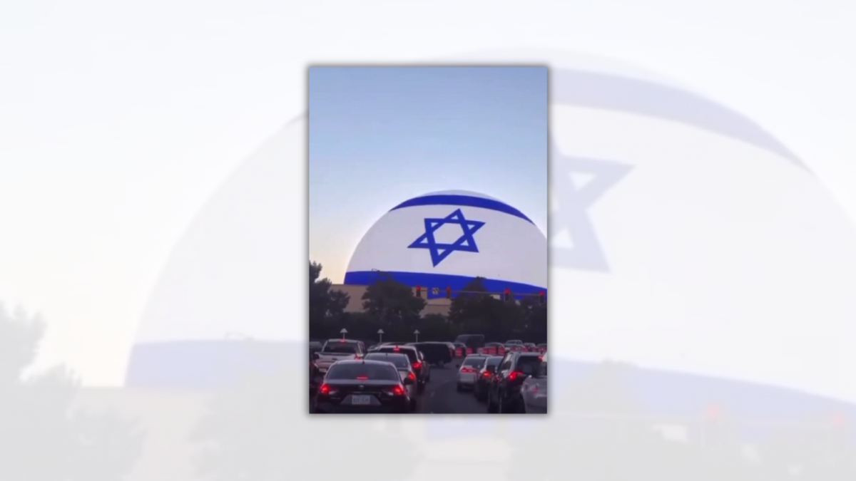 A screenshot of a video shows the flag of Israeli on a large sphere, with many cars in traffic below it. 