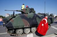 A man wrapped in a Turkisf flag walks past a military vehicle in front of Sabiha Airport, in Istanbul, Turkey July 16, 2016. REUTERS/Baz Ratner