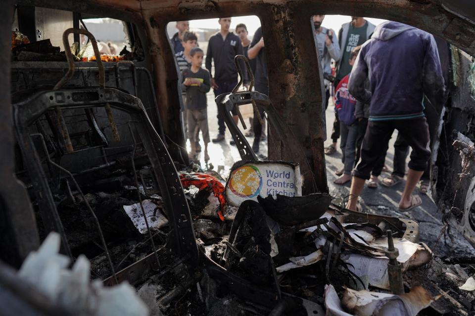 People gather around the remains of a car used by World Central Kitchen in the Gaza Strip on Tuesday. The U.S.-based aid group is pausing its Gaza operations after seven of its staff were killed in a "targeted Israeli strike."