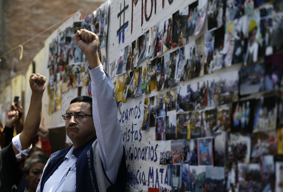 A man holds his fist in the air in front of photographs from the rescue efforts, during a minute of silence at Alvaro Obregon 286, where 49 died when their office building collapsed in last year's 7.1 magnitude earthquake, in Mexico City, Wednesday, Sept. 19, 2018. Across the city, memorials were held at sites where hundreds perished in the Sept. 19, 2017 quake.(AP Photo/Rebecca Blackwell)