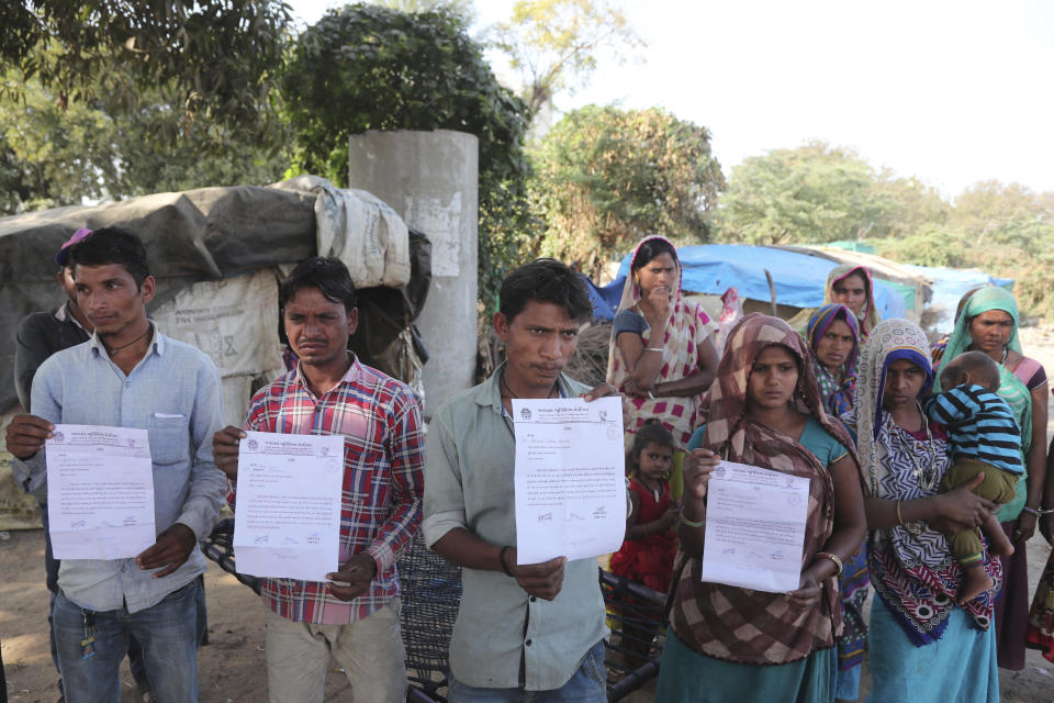 FILE - In this Tuesday, Feb. 18, 2020, file photo, residents of a slum near Sardar Patel Gujarat Stadium hold eviction notices served to them ahead of the visit of U.S. President Donald Trump in Ahmedabad, India. To welcome Trump, who last year likened Modi to Elvis Presley for his crowd-pulling power at a rally in Houston, the Gujarat government has spent almost $14 million on ads blanketing the city that show the two leaders holding up their hands, flanked by the Indian and U.S. flags. It also scrambled to build a wall to hide a slum from the road Trump and first lady Melania Trump will travel, caught stray dogs, planted exotic trees and is rushing to finish a cricket stadium in time for Trump’s arrival. (AP Photo/Ajit Solanki, File)