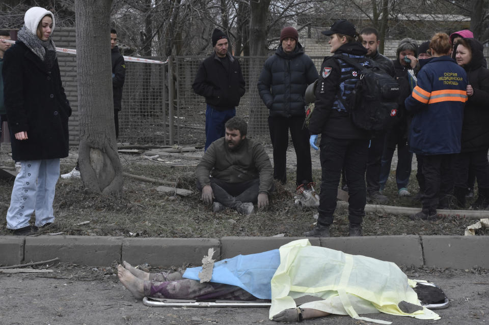 People react standing near the body of a resident killed in Russia's air attack in Zaporizhzhia, Ukraine, Friday, Dec. 29, 2023. (AP Photo/Andriy Andriyenko)