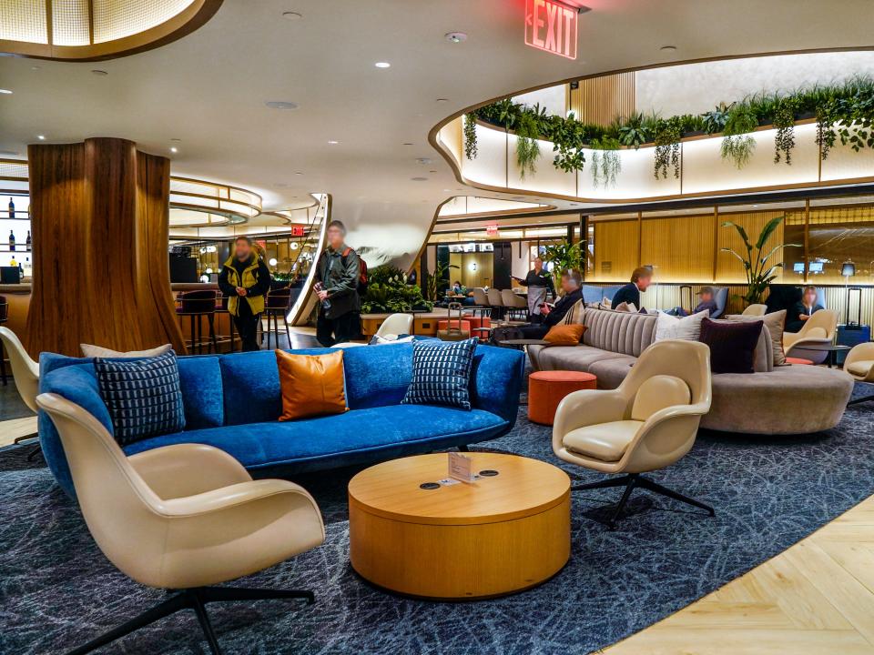 Inside a lounge with seveeral seating areas and hanging plants from a mezzanine.