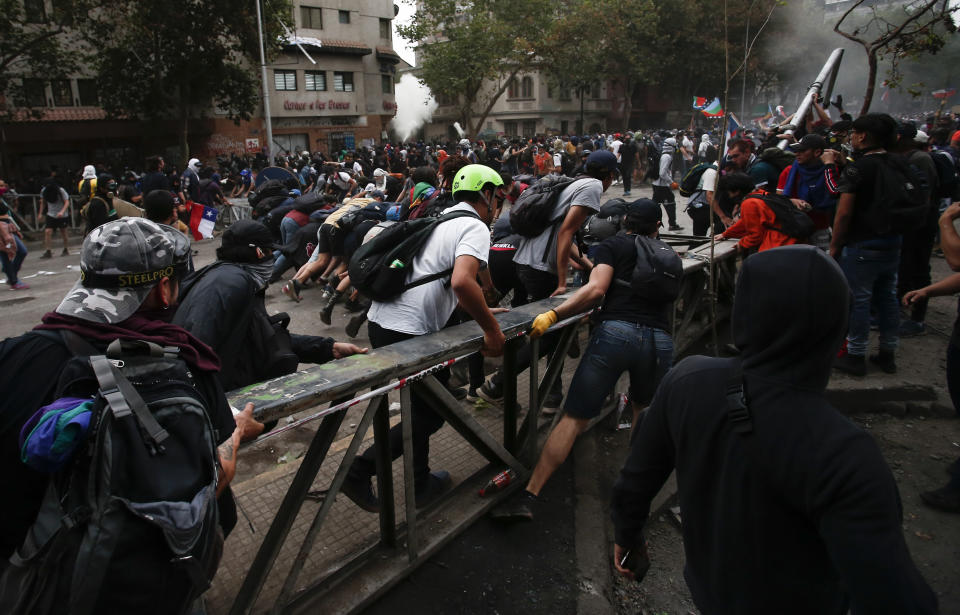 Anti-government protesters run with a metallic structure in Santiago, Chile, Friday, Nov. 8, 2019. Chile's president on Thursday announced measures to increase security and toughen sanctions for vandalism following three weeks of protests that have left at least 20 dead. (AP Photo/Luis Hidalgo)