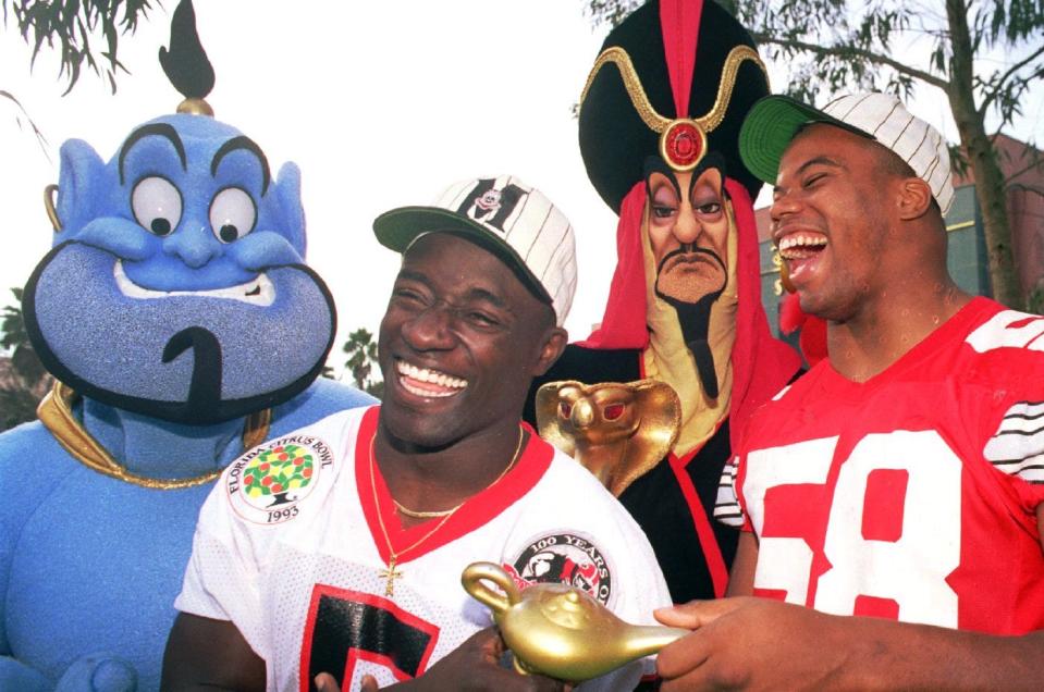 (DO102)LAKE BUENA VISTA, FLA., DEC. 24--CITRUS BOWL WISH--Garrison Hearst, left, of the University of Georgia, and Steve Tovar(58), of Ohio State University, share a laugh with characters from the movie Aladin as the two rub the magic lamp Thursday in Lake Buena Vista.   The players and their teamates were visiting Disney/MGM Studios and will meet in competition on January 1, 1993, in the Citrus Bowl in Orlando. (AP Photo)c (JR51705mbr/John Raoux-Orlando Sentinel) 92