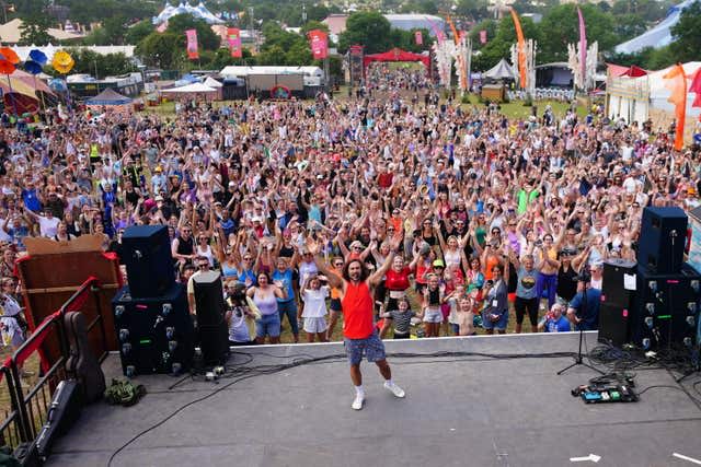 Jow Wicks raises his arms to the camera from the stage with the audience behind him