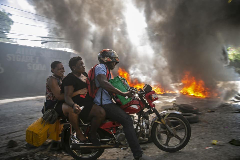 A moto-taxi driver takes two women past a burning barricade set up by people protesting fuel shortages in Petion-ville, Haiti, Sept. 15, 2019. The image was part of a series of photographs by Associated Press photographers which was named a finalist for the 2020 Pulitzer Prize for Breaking News Photography. (AP Photo/Dieu Nalio Chery)