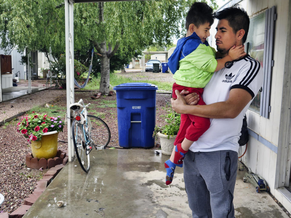 Osvaldo Salas, 29, stands with his son outside their home in suburban Phoenix on Wednesday, March 18, 2020. Salas, who isn't proficient in English, says he's disappointed state authorities haven't posted any information on the coronavirus in Spanish and that he has to rely on friends, family and TV for the latest. Salas, a restaurant cook, is worried about supporting his four children if he can't work anymore. (AP Photo/Astrid Galván)