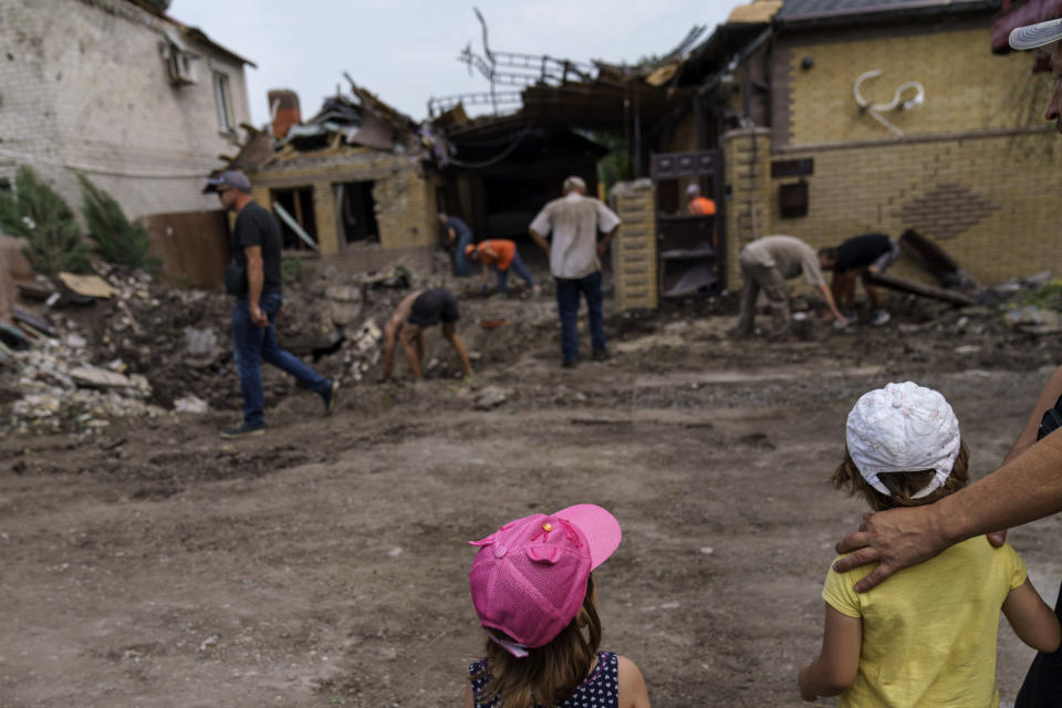 Children watch as workers clean up after a rocket strike on a house in Kramatorsk, Donetsk region, eastern Ukraine, Friday, Aug. 12, 2022. There were no injuries reported in the strike. (AP Photo/David Goldman)