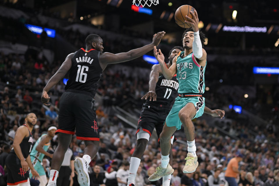 San Antonio Spurs' Tre Jones (33) goes to the basket against Houston Rockets' Usman Garuba (16) and Tari Eason during the second half of an NBA basketball game Thursday, Dec. 8, 2022, in San Antonio. (AP Photo/Darren Abate)