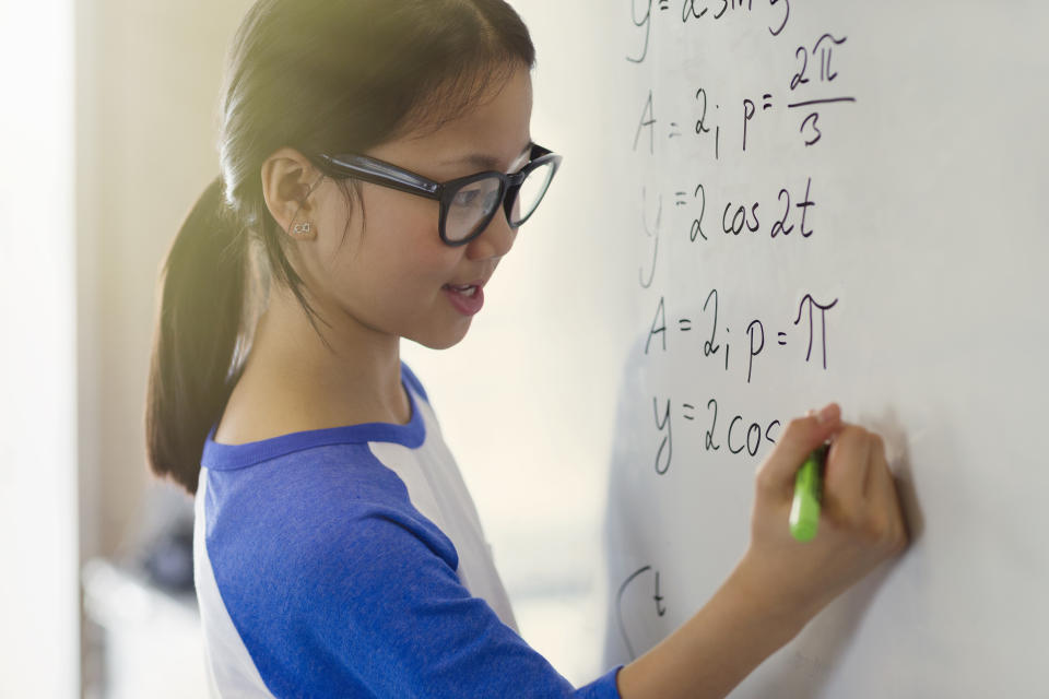 Girl solving physics equations on a classroom whiteboard.