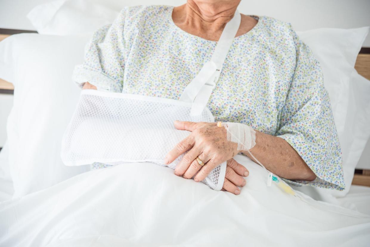 Broken arm of senior female patient sitting on bed in hospital