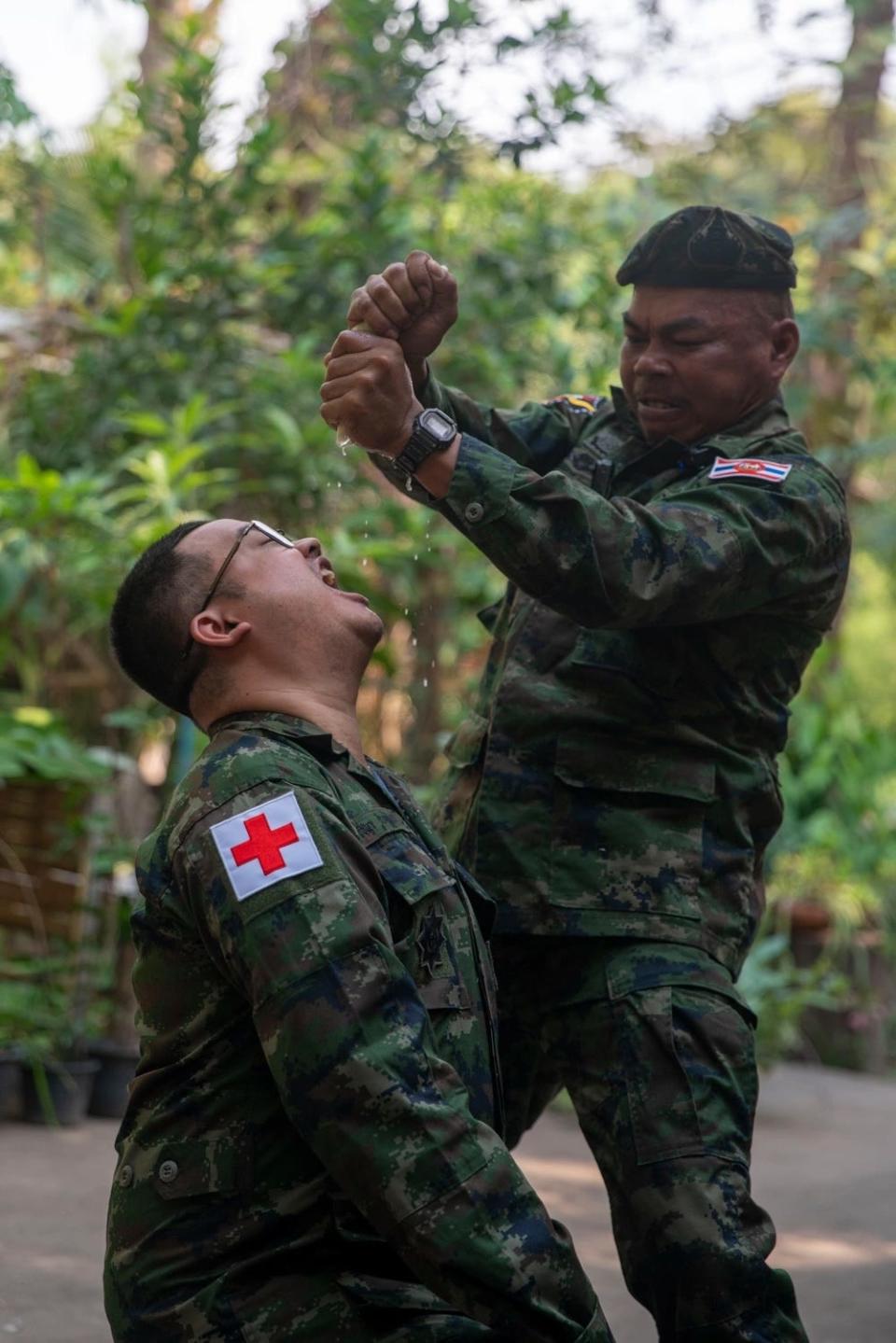 A Royal Thai Marine instructor squeezes water out of a plant into the mouth of a Marine