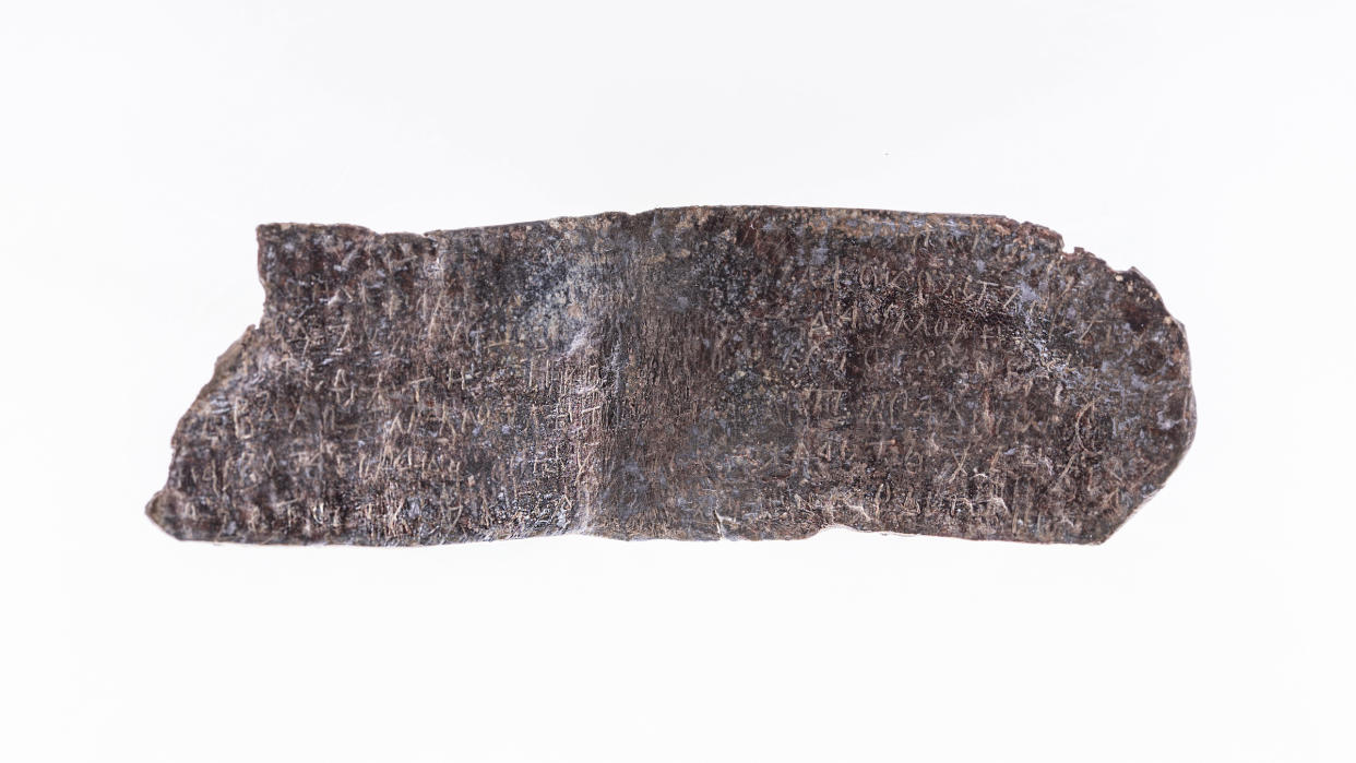  We see a horizontal finger-shaped lead piece with writing inscribed on it against a white background. 