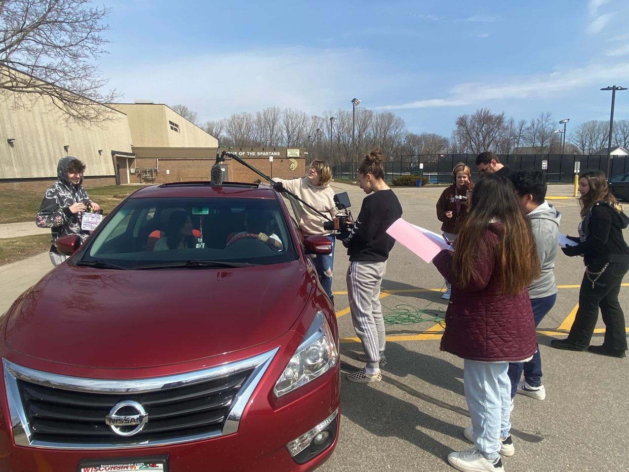 Students in the middle of production in Angela Brown's Movie Production class. From left to right: Brayden Kramlich, senior (holding clapboard); students in car: Avenna Yang, junior, and Junior Thao, junior; Atlas O'Hara, sophomore (holding boom mic); Kimi Binning, junior (holding camera); Namununa Vang, senior (holding pink paper); Sean Xiong, junior (student behind Namununa); Katie Sturtz, sophomore (student in all black).