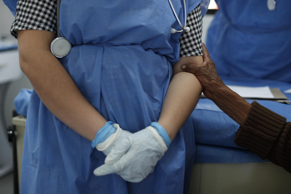 An elderly homeless woman clasps the arm of doctor Anahi Moreno during a routine health check-up in a mobile clinic run by the Ministry of Inclusion and Social Wellbeing, SIBISO, near the Basilica of Our Lady of Guadalupe in Mexico City, Wednesday, April 8, 2020. In an effort to combat the spread of the novel coronavirus, SIBISO has ramped up their mobile health clinic for the homeless from twice a week to daily, visiting additional locations and screening all comers for symptoms of COVID-19 in addition to routine health needs. (AP Photo/Rebecca Blackwell)