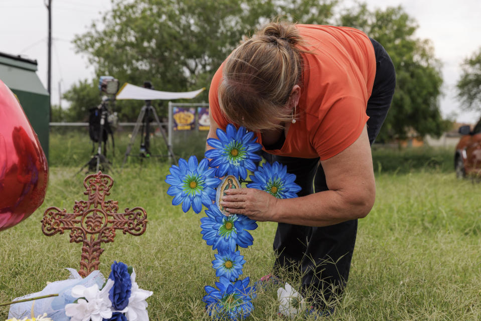 Rosario De La Cruz places a flower arrangement in the shape of a cross at a memorial site where eight migrants were killed and several others injured the day before while waiting at a bus stop in Brownsville, Texas, Monday, May 8, 2023. (AP Photo/Michael Gonzalez)