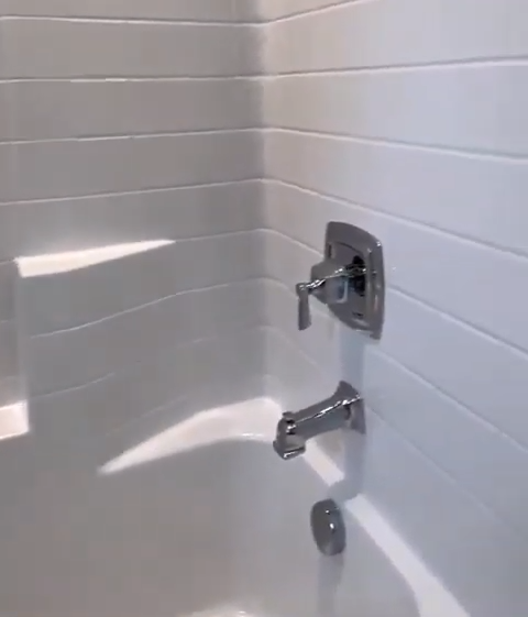 White-tiled bathroom corner with chrome faucet and showerhead, featuring @HDbuildersLLC watermark on the wall