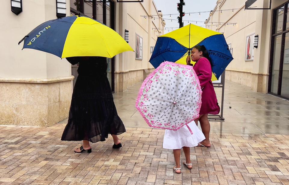 Customers shop in the rain during their visit to the Tanger Outlets in West Palm Beach, Florida on November 20, 2022. 