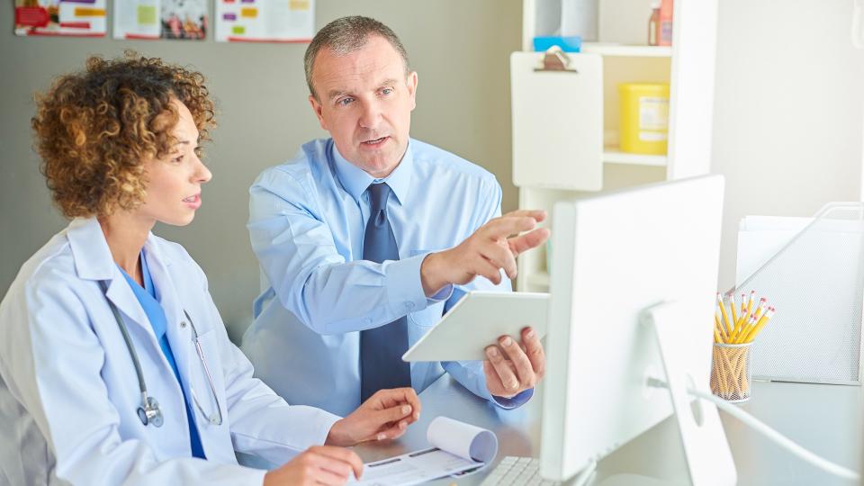 a medical salesman or administrator is sitting with a female doctor and running through a presentation .