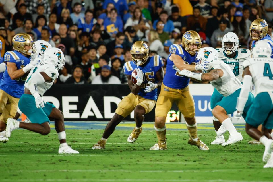 UCLA running back T.J. Harden carries the ball between Coastal Carolina defenders.