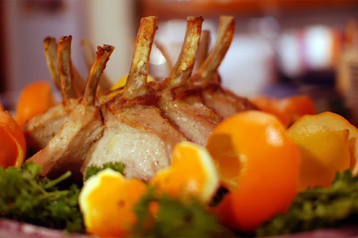 Closeup of crown roast of pork with onion and bread-crumb stuffing surrounded by orange peelings with a blurred background