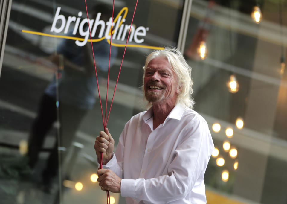 Richard Branson, of Virgin Group, prepares to unfurl a banner during a naming ceremony for the Brightline train station, to be renamed as Virgin MiamiCentral, Thursday, April 4, 2019, in Miami. The state's Brightline passenger trains are being renamed Virgin Trains USA after Branson invested in the new fast-rail project that is scheduled to connect Miami with Orlando. (AP Photo/Lynne Sladky)