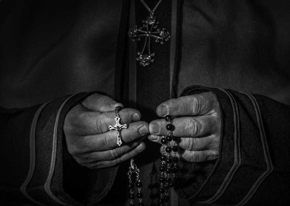 close up of priests hands holding rosary beads