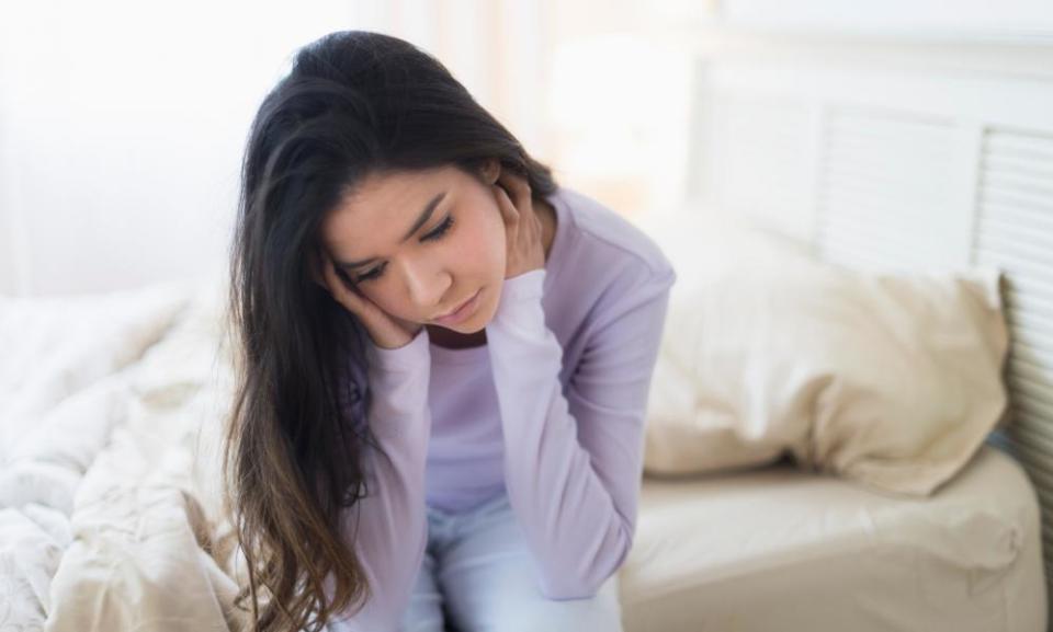 teenage girl sitting on her bed looking glum. A model posed for this image